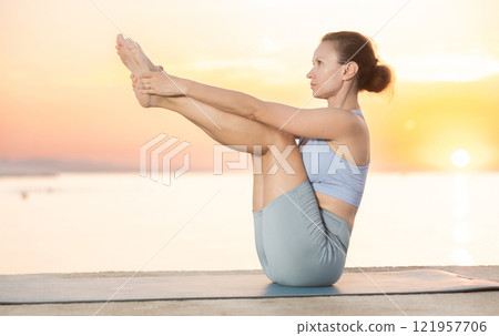 Near sea during sunset, girl performs boat pose 121957706