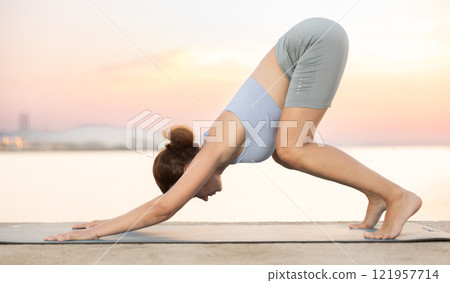 Near sea during sunset, girl performs Adho Mukha Svanasana Near sea during sunset, girl performs Adho Mukha Svanasana 121957714