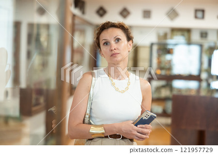 Historical museum - woman with smartphone in her hands looks at an exhibition of medieval sculptures and objects in historical museum 121957729