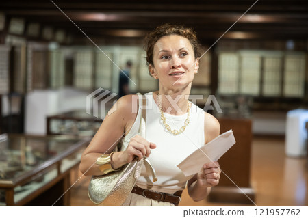 Woman curiously observing antique artifacts in historical museum Woman curiously observing antique artifacts in historical museum 121957762