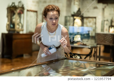 Woman with brochure in her hands examines exhibits in glass stands of historical museum 121957794