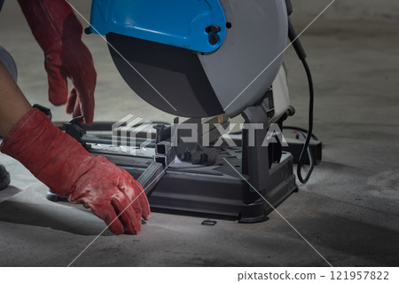 Worker cutting steel rectangular pipe in construction site. 121957822