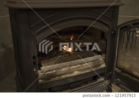 Image of lighting a wood stove with pine cones. 121957913
