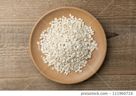 An overhead view of rolled barley on a wooden plate against a wood grain background 121960728