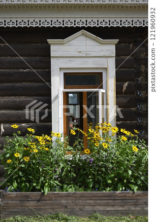 The windows of a 19th-century wooden house with architraves, wood carvings and daisies flowers 121960932