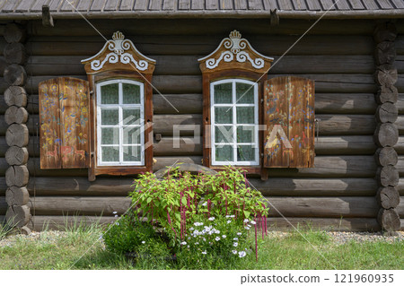 Windows of a 19th-century wooden house with wood carvings, painting on shutters and daisy flowers Windows of a 19th-century wooden house with wood carvings, painting on shutters and daisy flowers 121960935