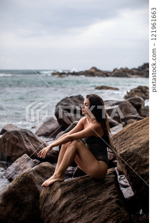 Serene Seaside Retreat A woman enjoying her time on a beautiful rocky shoreline by the ocean Serene Seaside Retreat A woman enjoying her time on a beautiful rocky shoreline by the ocean 121961663