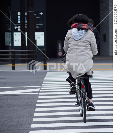 冬天,一名女子騎自行車穿過大城市十字路口的行人穿越道 冬天,一名女子騎自行車穿過大城市十字路口的行人穿越道 121961976