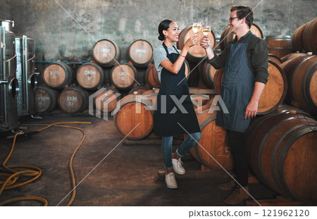 Wine distillery owners cheers glasses in the cellar standing by the barrels. Happy and celebrating business owners or sommeliers enjoying chardonnay or sauvignon blanc inside a winery 121962120
