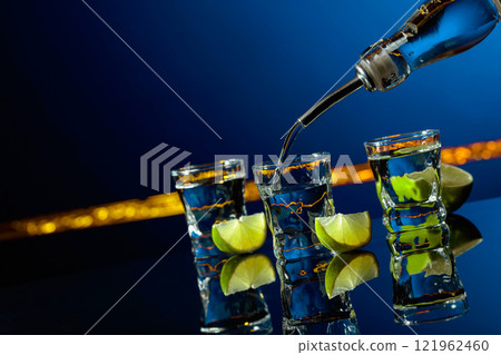 Strong alcoholic drink and lime slices on a dark blue background. Strong alcoholic drink and lime slices on a dark blue background. 121962460