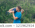 A joyful father enjoys a fun moment outdoors with his child in a lush natural environment, making memories 121962914