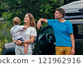 A joyful family happily enjoying their exciting outdoor adventure close to a vehicle, embraced by nature 121962916