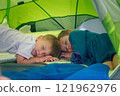 An adorable and heartwarming scene of two young kids peacefully sleeping inside a vibrant and colorful camping tent 121962976