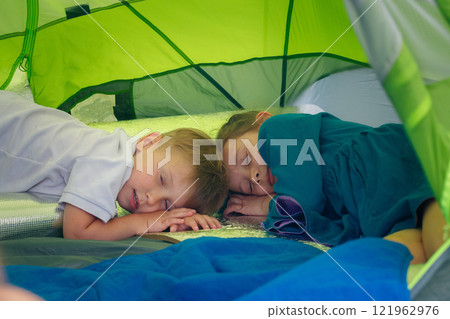 An adorable and heartwarming scene of two young kids peacefully sleeping inside a vibrant and colorful camping tent 121962976