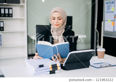 Young Arabic female entrepreneur wearing a hijab working  with a laptop Concentrated math finance on an office desk, tax, report, accounting, statistics 121963222