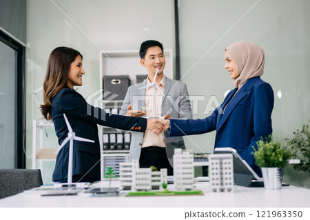 Group of diverse multiethnic businesspeople standing neare table looking at model of building from residential project. 121963350