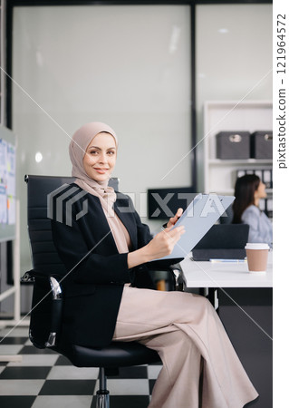 Young Arabic female entrepreneur wearing a hijab working online with a laptop at modern office 121964572