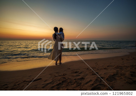 mother holding toddler baby girl on sea beach at sunset in Pattaya, Thailand 121965802