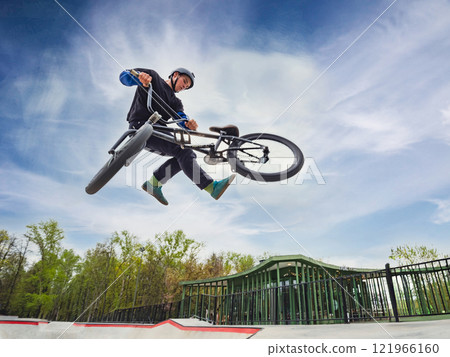 BMX bicycle rider doing stunt Tailwhip in quarter pipe. Skilled BMX freestyler athlete jumping over quarter ramp and doing aerial trick Tailwhip in street ramp park outdoors 121966160