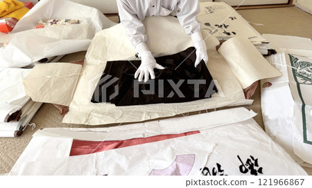 A woman's hand in white gloves assessing a black kimono on a wrapping paper_wide A woman's hand in white gloves assessing a black kimono on a wrapping paper_wide 121966867