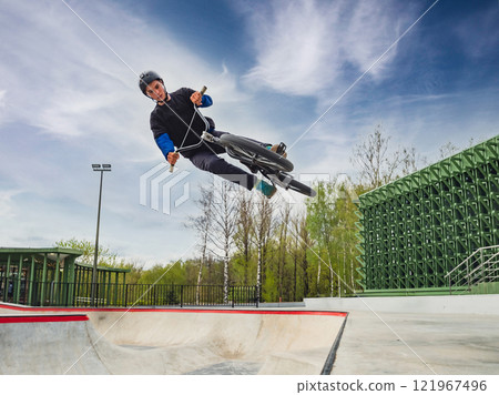 BMX bicycle rider doing stunt jump in quarter pipe. Skilled BMX freestyler athlete jumping over quarter ramp and doing aerial trick in street ramp park outdoors 121967496