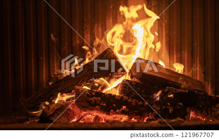 Stacked firewood burning brightly in a fireplace with vivid flames and glowing embers, creating a warm and inviting indoor ambiance. 121967707