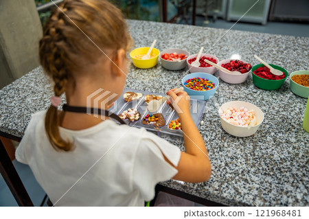 Little girl learning how to cook in a cooking class. Handmade dessert. Making chocolate candy, Child filling heart shaped mold with chocolate 121968481