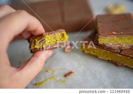 Piece of trend Dubai chocolate with pistachio paste and kataifi dough in woman hand. Confectionery handmade sweets at home in the kitchen.  121968488