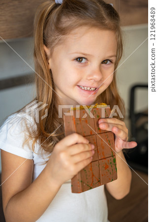 Little girl eating Dubai chocolate with pistachio paste and kataifi dough. Confectionery handmade sweets at home in the kitchen.  121968489