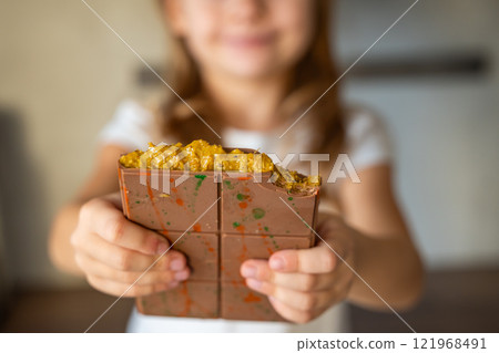 Dubai chocolate with pistachio paste and kataifi dough in hands of little girl. Confectionery handmade sweets at home in the kitchen. Dubai chocolate with pistachio paste and kataifi dough in hands of little girl. Confectionery handmade sweets at home in the kitchen. 121968491