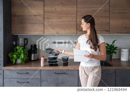 Young woman with healthy diet plan for weight loss, delivery of daily ready meal menu. Food ordered with mobile phone app. Balanced portion with dish. Pre-cooking. 121968494