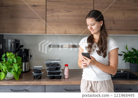 Young woman with healthy diet plan for weight loss, delivery of daily ready meal menu. Woman using meal tracker app on phone. Balanced portion with dish. Pre-cooking. Young woman with healthy diet plan for weight loss, delivery of daily ready meal menu. Woman using meal tracker app on phone. Balanced portion with dish. Pre-cooking. 121968495