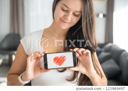 World Health Day concept. Young woman showing illustration of heart on her smartphone, illustrating the importance of cardiovascular health awareness on international health observation World Health Day concept. Young woman showing illustration of heart on her smartphone, illustrating the importance of cardiovascular health awareness on international health observation 121968497
