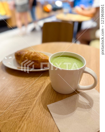Cup of matcha latte and a croissant on a wooden table in a cozy cafe or coffee shop. Warmth and comfort of a morning or afternoon break. 121968661