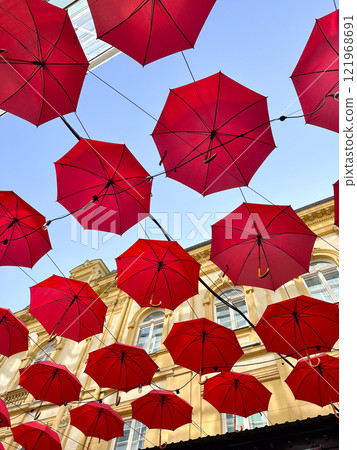 Red umbrellas suspended against a clear blue sky, whimsical and artistic atmosphere. Fusion of creativity and urban architecture, design exterior of outdoor restaurant and hotel. 121968691
