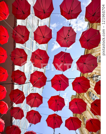 Red umbrellas suspended against a clear blue sky, whimsical and artistic atmosphere. Fusion of creativity and urban architecture, design exterior of outdoor restaurant and hotel. Red umbrellas suspended against a clear blue sky, whimsical and artistic atmosphere. Fusion of creativity and urban architecture, design exterior of outdoor restaurant and hotel. 121968704