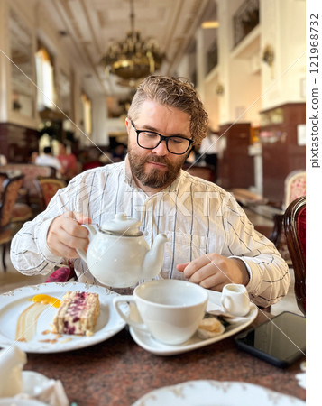 Portrait bearded man enjoying an elegant tea break in a luxurious cafe with classical decor. Luxury restaurant paired with fine tableware and a slice of cake, timeless and refined atmosphere Portrait bearded man enjoying an elegant tea break in a luxurious cafe with classical decor. Luxury restaurant paired with fine tableware and a slice of cake, timeless and refined atmosphere 121968732