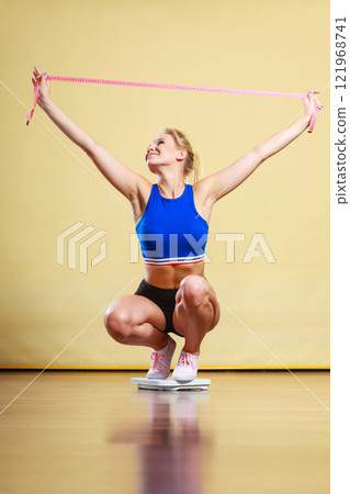Joyful girl standing on bathroom scales Joyful girl standing on bathroom scales 121968741