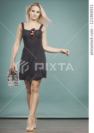 Woman wearing short dress holding flip flops and sunglasses Woman wearing short dress holding flip flops and sunglasses 121968931