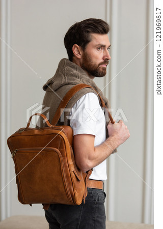 A Stylish and Man standing with a yellow brown backpack in a Contemporary Modern Setting A Stylish and Man standing with a yellow brown backpack in a Contemporary Modern Setting 121969817
