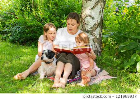Mother reading book to daughters outdoors with pet dog Mother reading book to daughters outdoors with pet dog 121969937