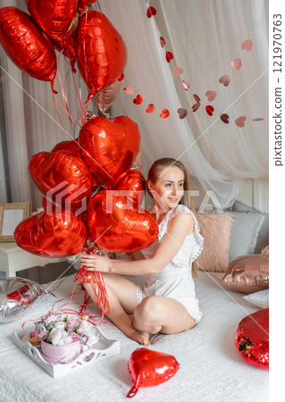 Beautiful young girl at home on the bed in the morning enjoy valentines day celebration with heart shaped balloons Beautiful young girl at home on the bed in the morning enjoy valentines day celebration with heart shaped balloons 121970763