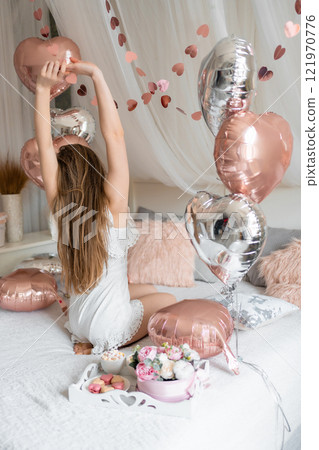 Beautiful young girl at home on the bed in the morning enjoy valentines day celebration with heart shaped balloons Beautiful young girl at home on the bed in the morning enjoy valentines day celebration with heart shaped balloons 121970776