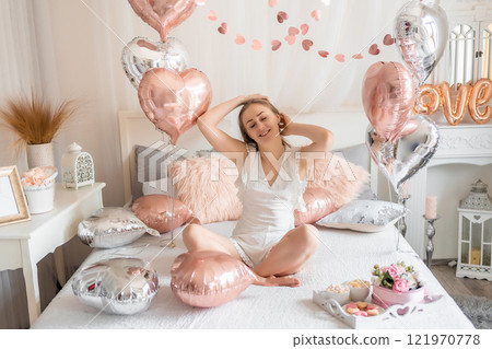 Beautiful young girl at home on the bed in the morning enjoy valentines day celebration with heart shaped balloons Beautiful young girl at home on the bed in the morning enjoy valentines day celebration with heart shaped balloons 121970778