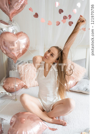 Beautiful young girl at home on the bed in the morning enjoy valentines day celebration with heart shaped balloons Beautiful young girl at home on the bed in the morning enjoy valentines day celebration with heart shaped balloons 121970786