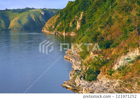 Calm river.Rocky warm hills overgrown with trees and greenery 121971252