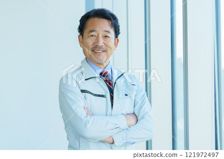 A middle-aged man in work clothes standing in front of an office window. Photo courtesy of Tokyo Electronics College, Denpa Gakuen Corporation. 121972497