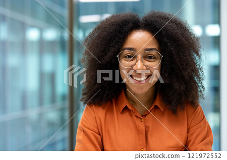 Close-up portrait of a young successful businesswoman at her workplace inside the office. Office worker smiling looking at the camera. Close-up portrait of a young successful businesswoman at her workplace inside the office. Office worker smiling looking at the camera. 121972552