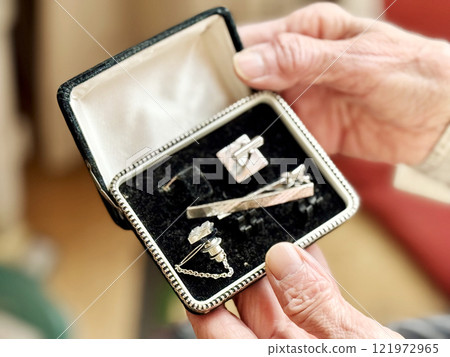 一位老婦人打開一個盒子，裡面有一套舊袖扣和領帶夾 121972965