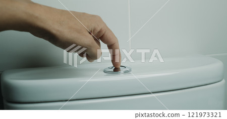 man flushing the toilet in a white-tiled bathroom man flushing the toilet in a white-tiled bathroom 121973321